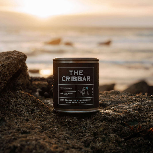 The Cribbar soy candle by Kernowfornia Soul, handmade in Cornwall and ocean-scented, glowing in golden sunset light beside deep blue sea at Newquay’s Cribbar reef—eco friendly and clean burning gift for surfers.