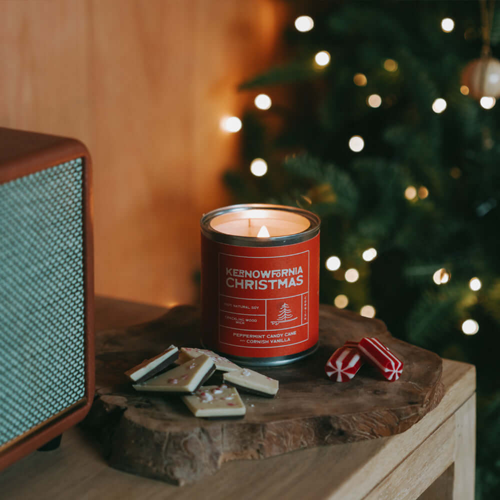 Candle labeled 'Kenowlnia Christmas' on a wooden surface with a festive background