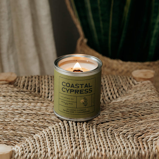 Warm lit wooden wick Cypress scented candle styled with natural fabrics and foliage in a beach-inspired bathroom, perfect vegan candle for coastal home interiors