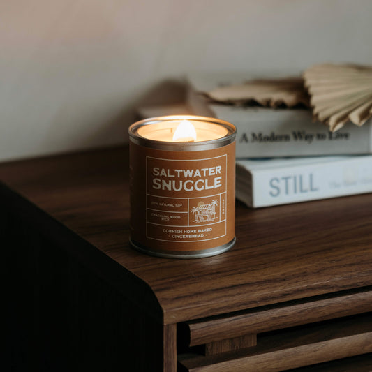warm glowing Saltwater Snuggle soy candle on a retro wooden side table in a cozy Cornish cottage with coastal living books in the background— eco soy candle for relaxing home vibes