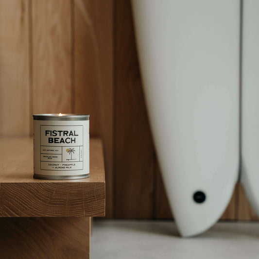 Eco-friendly wooden wick soy candle from Kernowfornia Soul lit indoors on wooden step, surfboard in soft focus behind, reflecting beach and surf vibes
