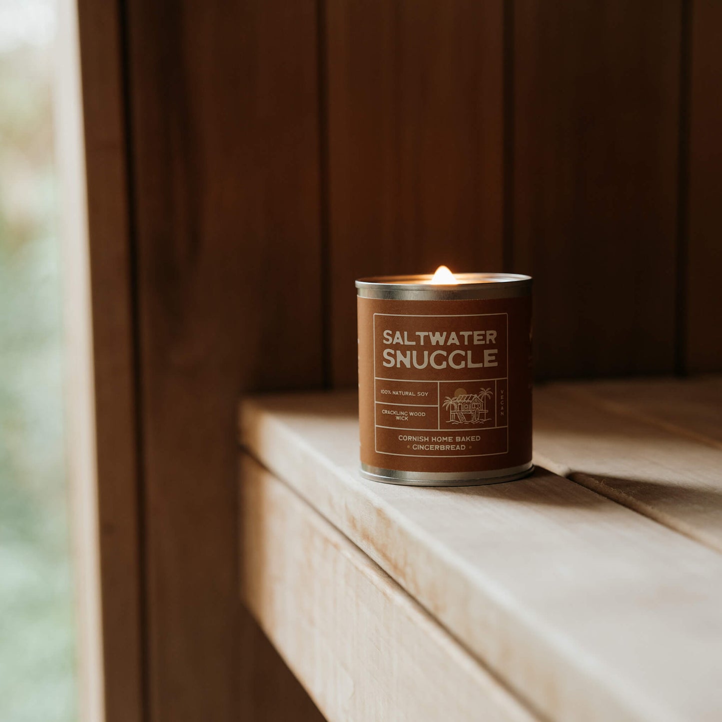 Saltwater Snuggle gingerbread scented soy candle glowing inside rustic wood sauna, surrounded by nature – eco-friendly vegan candle inspired by Cornish coastal living