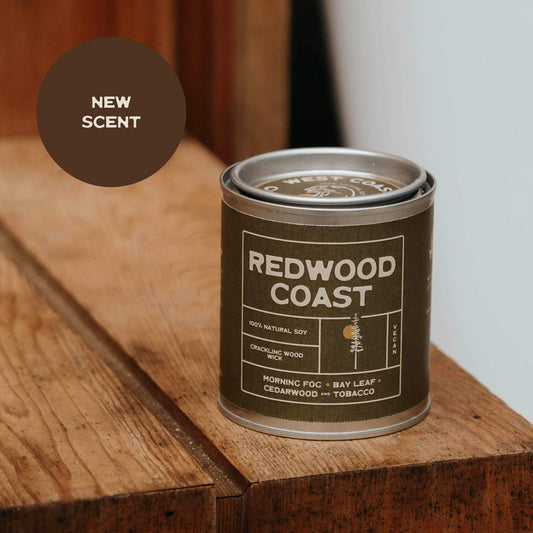 Redwood Coast candle in a tin on a wooden surface with 'New Scent' label.