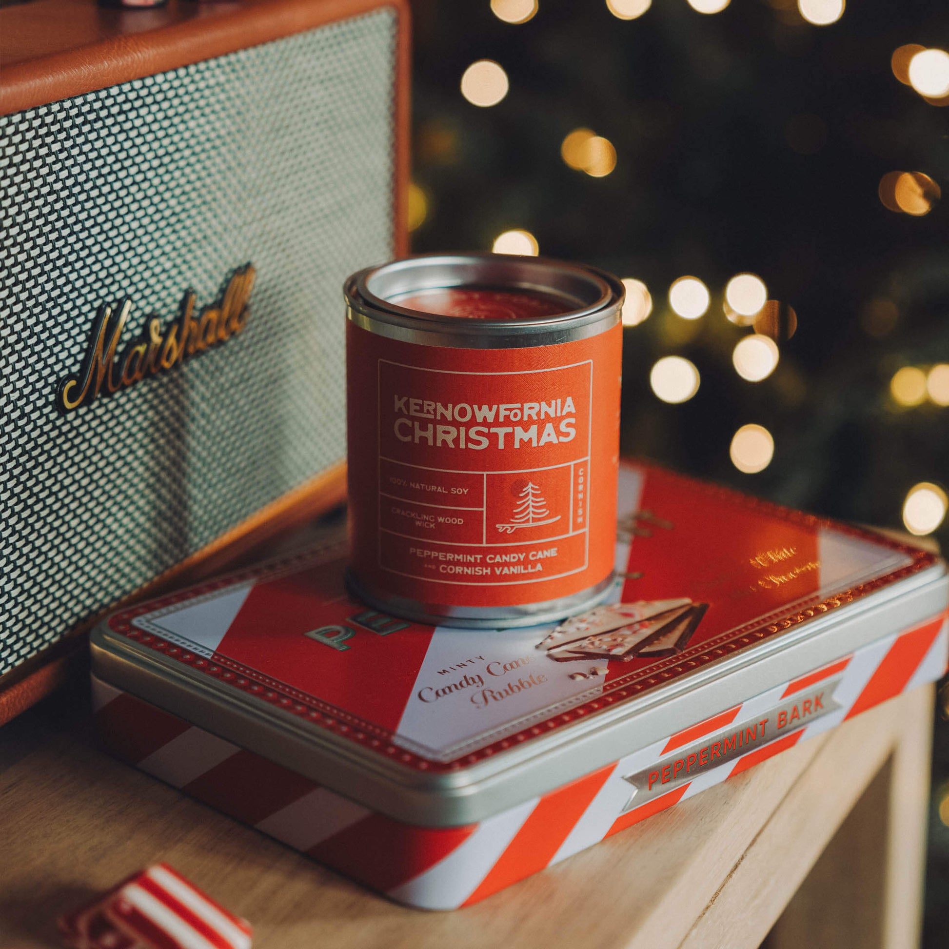 Red and white striped tin with a can of 'Kernewkarn Christmas' on a wooden surface with a Marshall amplifier in the background.