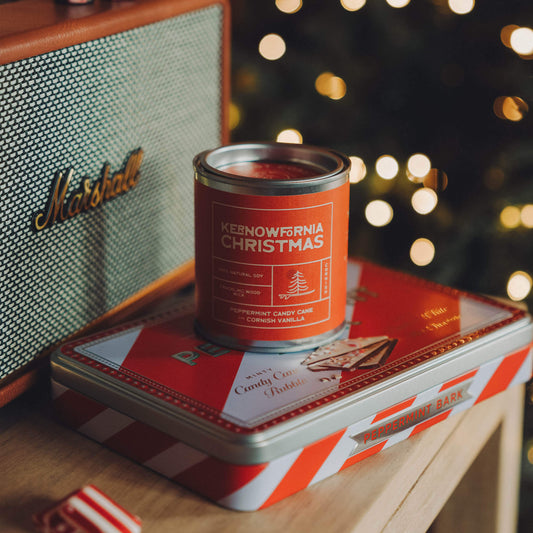 Red and white striped tin with a can of 'Kernewkarn Christmas' on a wooden surface with a Marshall amplifier in the background.