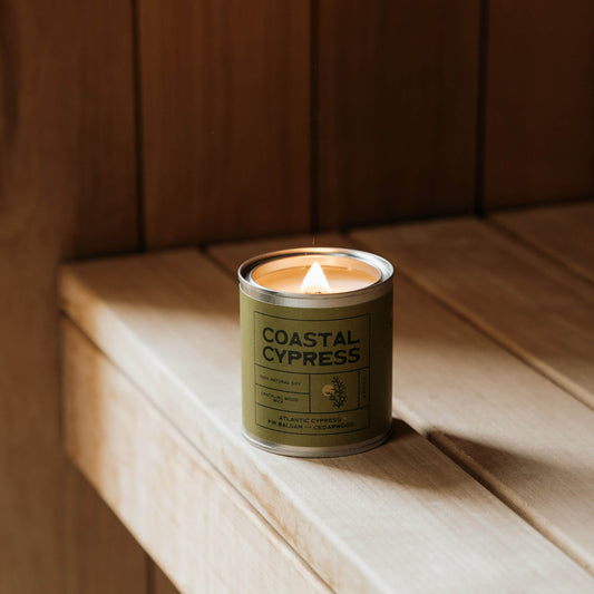 Coastal Cypress scented soy candle glowing inside rustic wood sauna, surrounded by nature – eco-friendly vegan candle inspired by forest and coastal living