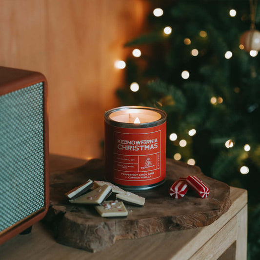Candle labeled 'Kenowlnia Christmas' on a wooden surface with a festive background