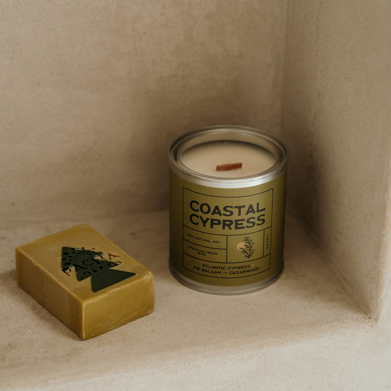 Rich green Coastal Cypress scented candle beside vegan olive soap on modern shelf, showcasing eco-friendly coastal candle in serene luxury bathroom