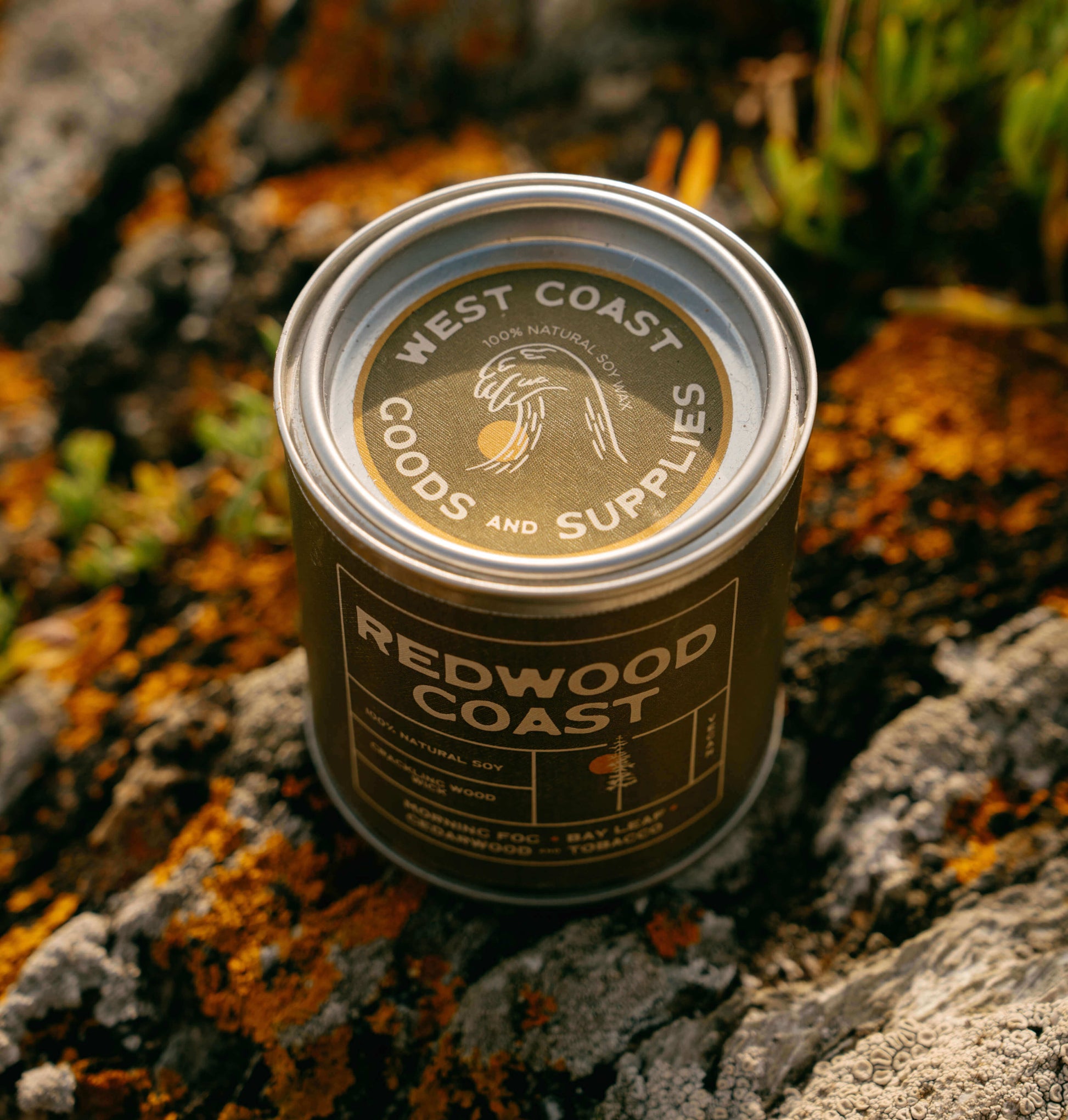 Candle in a metal tin labelled redwood coast, on the rugged coast of California.  